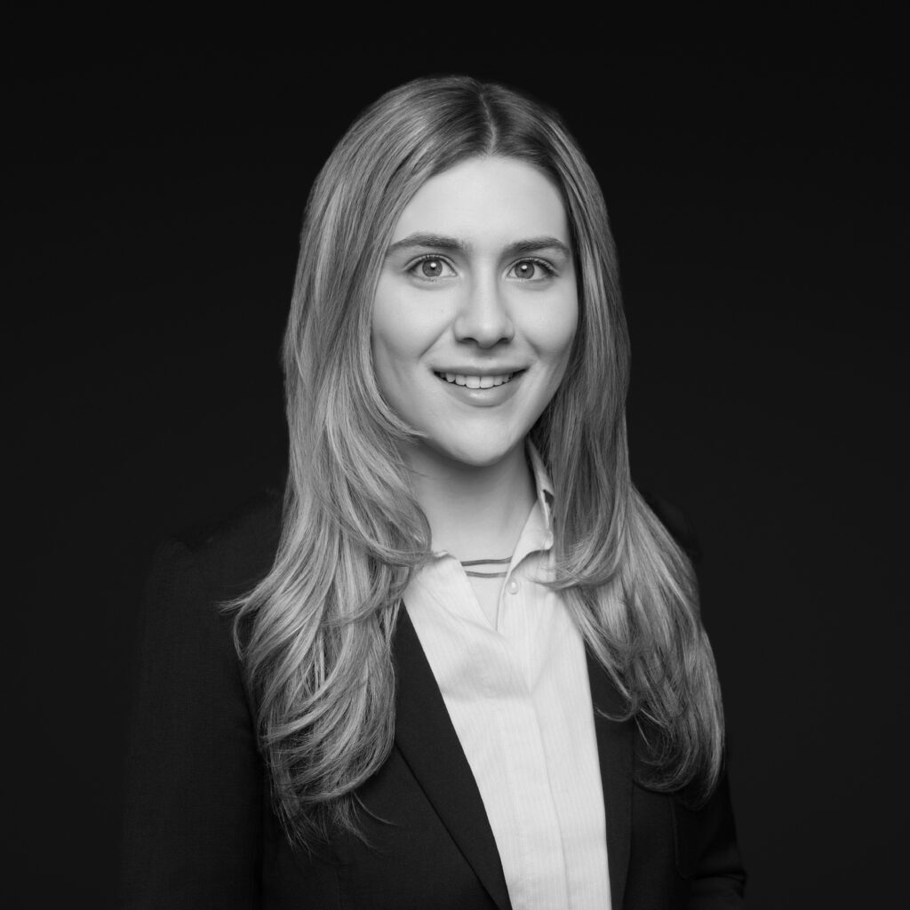 A woman with long, fair hair is wearing a suit jacket and a buttoned-up shirt, smiling at the camera against a plain dark background in a black and white portrait. Unified LLP | Toronto T. 416.787.7678 | Kitchener T. 519.729.5038 | Calgary T. 403-906-2351 | unifiedllp.com