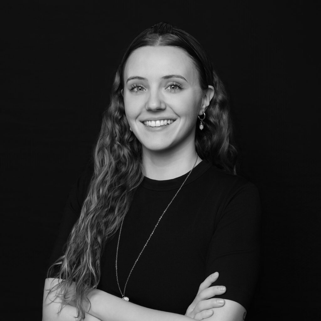 A woman with long wavy hair, wearing a black shirt and a necklace, stands with her arms folded and smiles at the camera against a plain black background. Unified LLP | Toronto T. 416.787.7678 | Kitchener T. 519.729.5038 | Calgary T. 403-906-2351 | unifiedllp.com