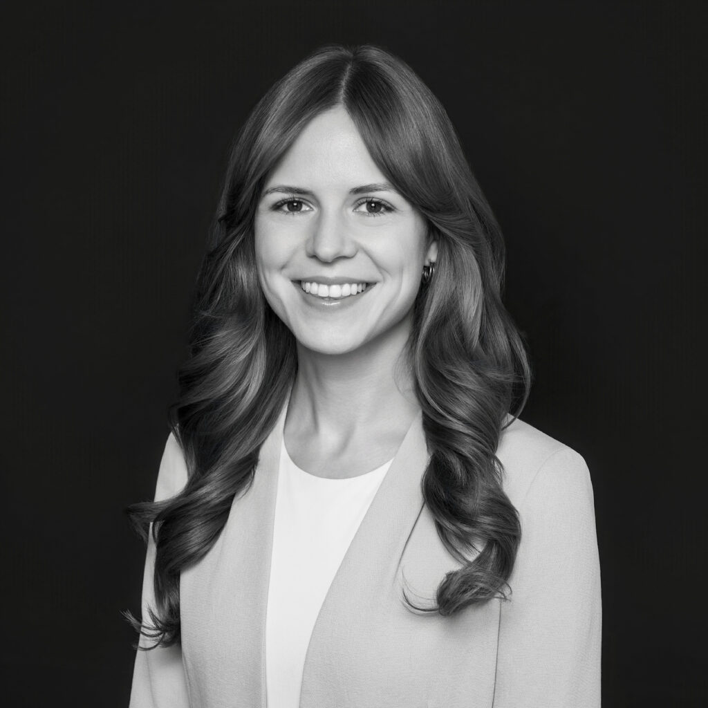 A woman with long, wavy hair wearing a light-coloured blazer and white top smiles at the camera against a plain dark background. The photo is in black and white. Unified LLP | Toronto T. 416.787.7678 | Kitchener T. 519.729.5038 | Calgary T. 403-906-2351 | unifiedllp.com