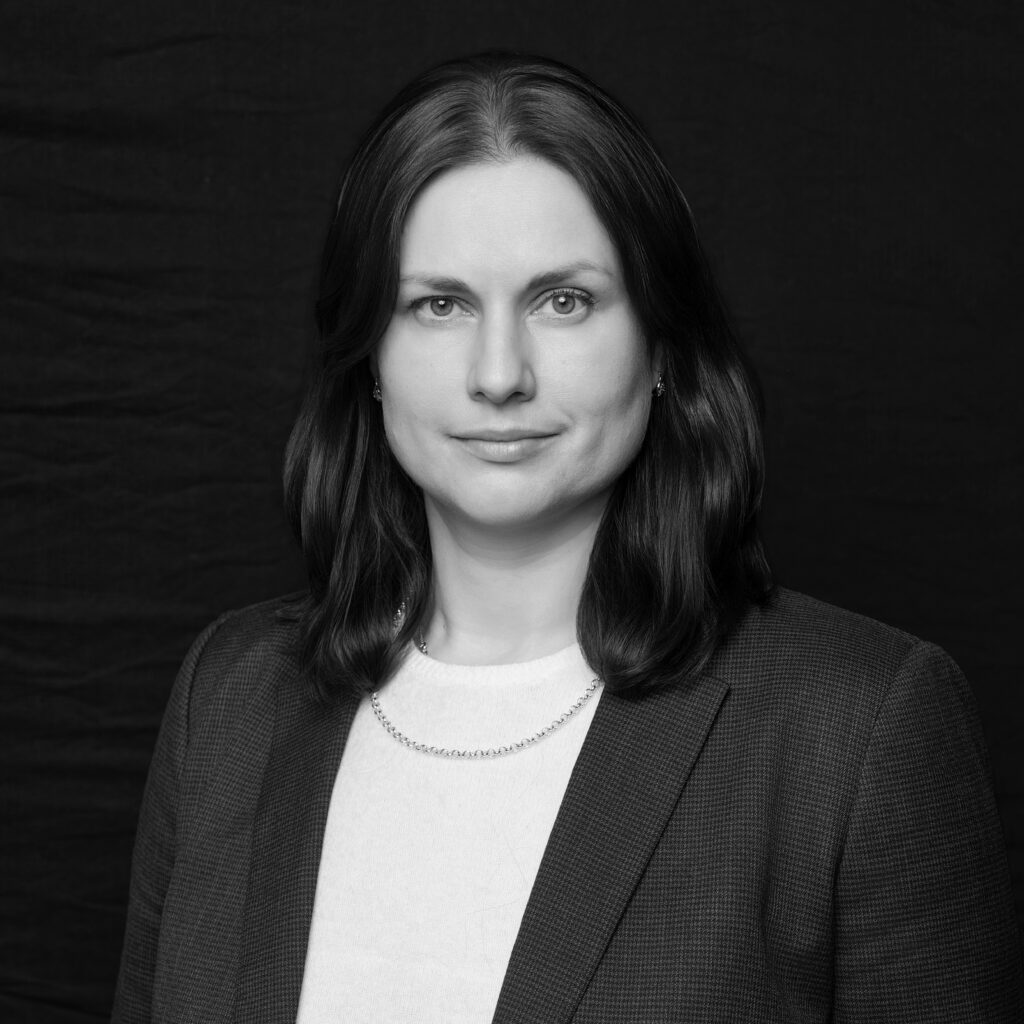 A woman with shoulder-length dark hair wearing a blazer, light top, and chain necklace poses against a plain dark background. She looks directly at the camera with a neutral expression. The image is in black and white. Unified LLP | Toronto T. 416.787.7678 | Kitchener T. 519.729.5038 | Calgary T. 403-906-2351 | unifiedllp.com