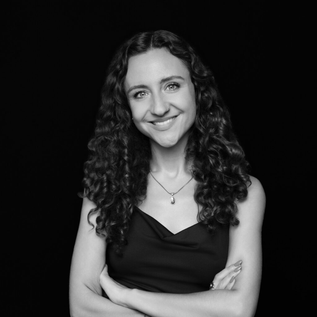 Jillian, a Toronto employment lawyer with long curly hair, wearing a sleeveless top and a necklace, stands with arms folded, smiling at the camera against a black background. Unified LLP | Toronto T. 416.787.7678 | Kitchener T. 519.729.5038 | Calgary T. 403-906-2351 | unifiedllp.com