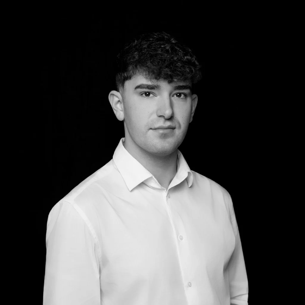 A person with short curly hair, wearing a light-coloured button-up shirt, faces the camera against a plain black background. The image is in black and white. Unified LLP | Toronto T. 416.787.7678 | Kitchener T. 519.729.5038 | Calgary T. 403-906-2351 | unifiedllp.com