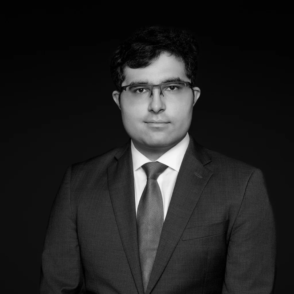 A man wearing glasses, a suit, and a tie poses against a plain, dark background. The image is black and white, and he is looking straight at the camera with a neutral expression. Unified LLP | Toronto T. 416.787.7678 | Kitchener T. 519.729.5038 | Calgary T. 403-906-2351 | unifiedllp.com