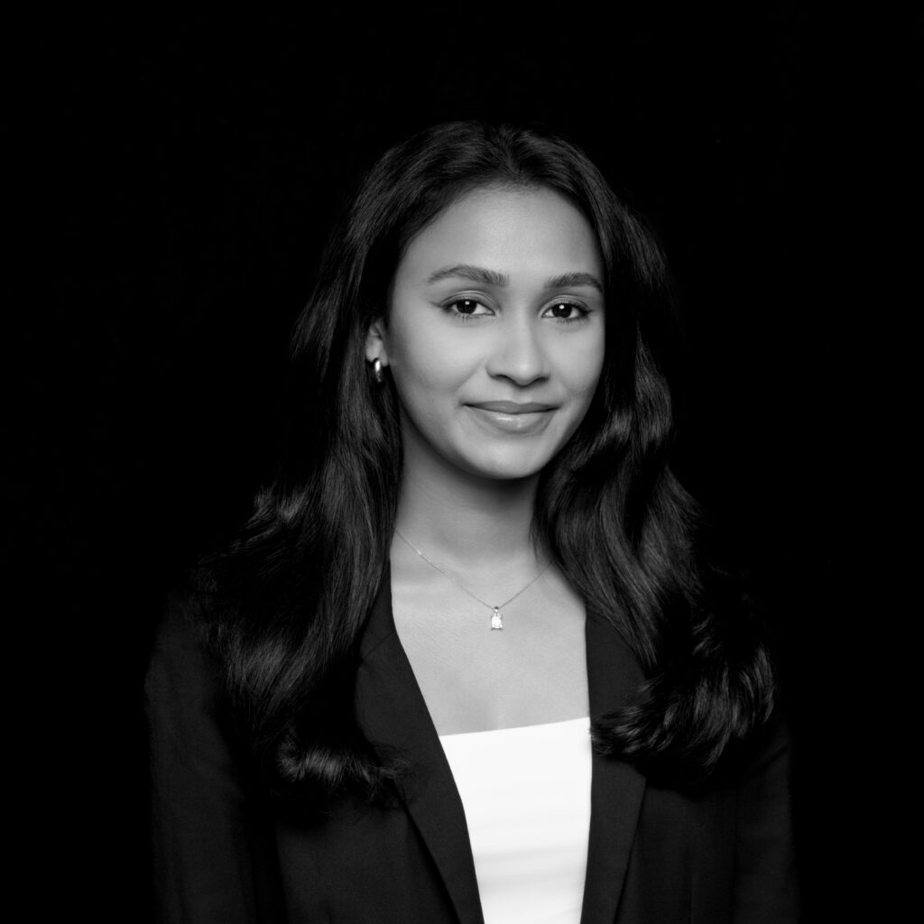 A woman with long dark hair, wearing a blazer over a light top and a small pendant necklace, is shown against a solid black background. She is looking at the camera with a neutral expression. The image is in black and white. Unified LLP | Toronto T. 416.787.7678 | Kitchener T. 519.729.5038 | Calgary T. 403-906-2351 | unifiedllp.com