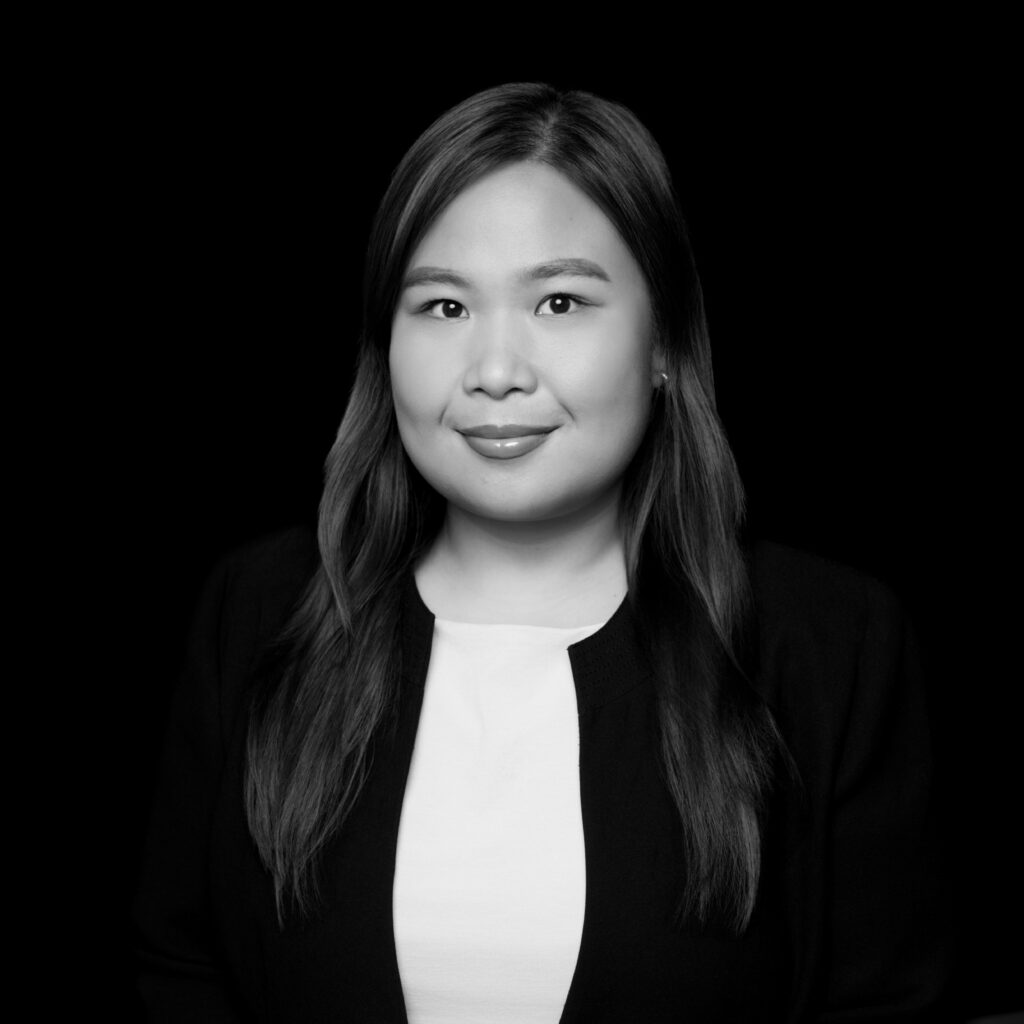 A woman with long, straight hair is wearing a light-coloured top and a dark blazer. She is facing forward and smiling slightly. The background is solid black. The image is in black and white. Unified LLP | Toronto T. 416.787.7678 | Kitchener T. 519.729.5038 | Calgary T. 403-906-2351 | unifiedllp.com